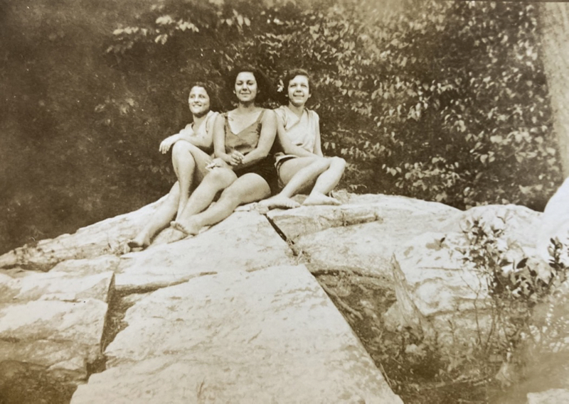 Photo of Esther and two other young women, in swimsuits, sitting on rocks, smiling
